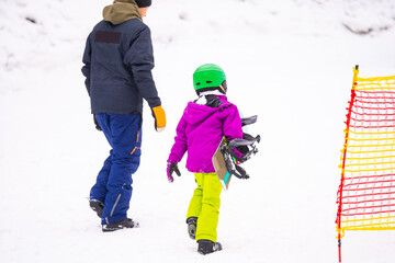 Fototapeta na wymiar At Cold Winder Day at Mountain Ski Resort Father Teaching Little Daughter Snowboarding
