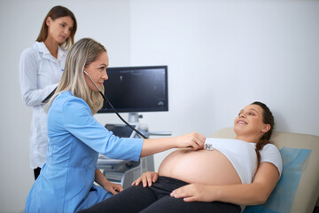 Docotor doing diagnostic with stethoscope for pregnant woman