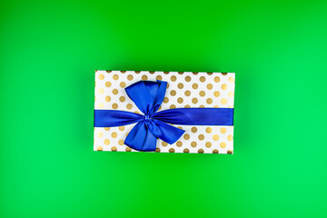 A gift wrapped in white paper with gold circles wrapped in a blue ribbon tied in a bow, isolated on a green background, top view.