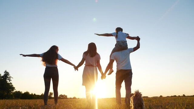 people in the park. happy family silhouette walk at sunset. mom dad and daughters walk holding hands in park. happy family lifestyle kid dream concept. parents and children walking back silhouette