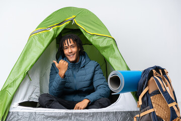 Young african american man inside a camping green tent pointing to the side to present a product