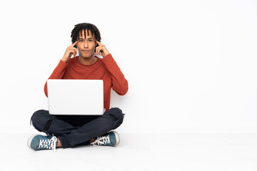 Young african american man sitting on the floor and working with his laptop having doubts and thinking
