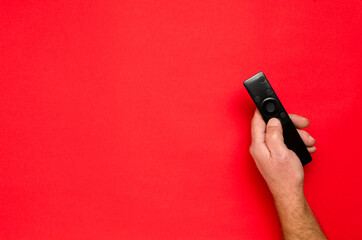Top view of male hand, black tv clicker for smart television onth red surface.Empty space