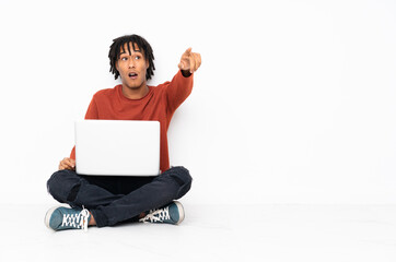 Young african american man sitting on the floor and working with his laptop pointing away