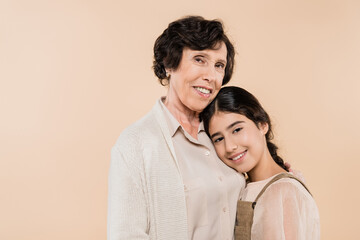 Fototapeta premium Elderly hispanic woman hugging granddaughter isolated on beige, two generations of women