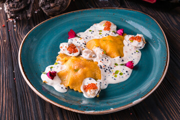 Ravioli with crab in caviar sauce on a large turquoise plate. The plate stands on a wooden table and is draped with a light cloth.