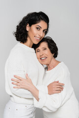 Positive hispanic woman embracing elderly mother isolated on grey, two generations of women
