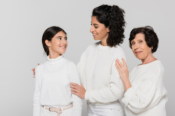 Hispanic girl looking at mother near smiling grandma isolated on grey, three generations of women