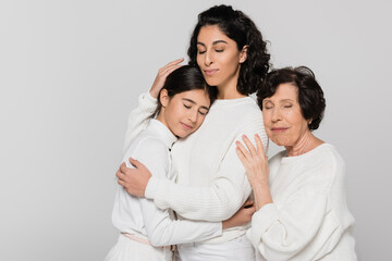 Obraz premium Three generations of hispanic women hugging with closed eyes isolated on grey