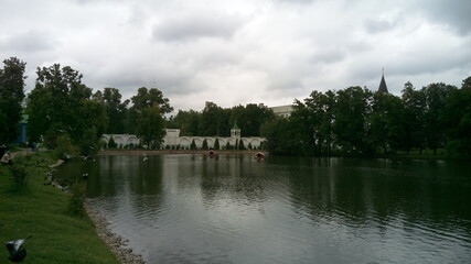 The gray surface of the lake with reflected clouds and white buildings hidden behind green trees