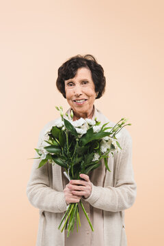 Elderly hispanic woman holding bouquet isolated on beige