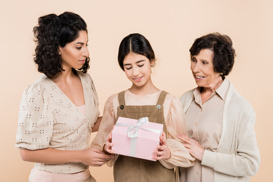 Smiling Hispanic Child Holding Gift Box Near Mother And Grandmother Isolated On Beige, Three Generations Of Women