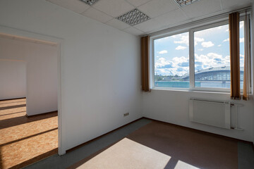 Modern interior of empty office room. White walls and door. Huge window with vertical blinds. Sunny day.