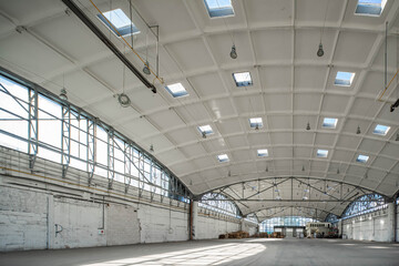 Stack wooden pallets in huge empty industrial warehouse. White interior. Hemispherical reinforced concrete load bearing roof with windows. Modern architecture.