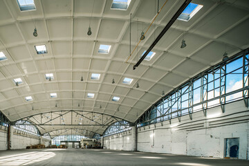 Stack wooden pallets in huge empty industrial warehouse. White interior. Hemispherical reinforced concrete load bearing roof with windows. Modern architecture.