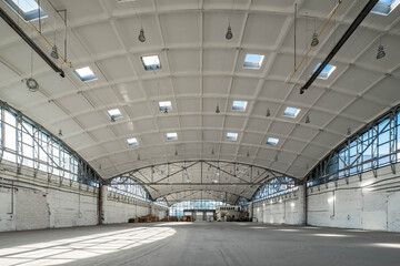 Stack wooden pallets in huge empty industrial warehouse. White interior. Hemispherical reinforced concrete load bearing roof with windows. Modern architecture.