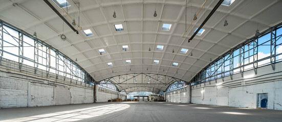 Stack wooden pallets in huge empty industrial warehouse. White interior. Hemispherical reinforced concrete load bearing roof with windows. Modern architecture.