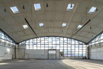 Huge empty industrial warehouse. White interior. Unique architecture. Hemispherical reinforced concrete load bearing roof with windows. Modern building.