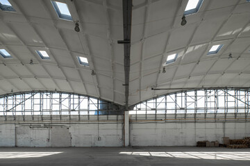 Huge empty industrial warehouse. White interior. Unique architecture. Hemispherical reinforced concrete load bearing roof with windows. Wooden pallets near wall.