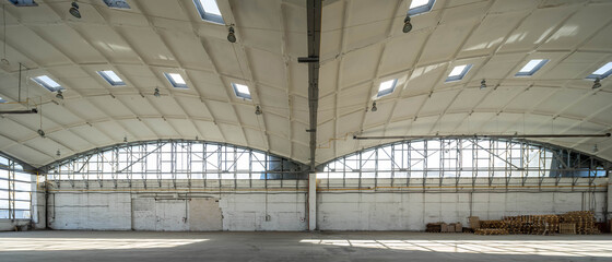 Huge empty industrial warehouse. White interior. Unique architecture. Hemispherical reinforced concrete load bearing roof with windows. Wooden pallets near wall.