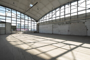Huge empty industrial warehouse. White interior. Unique architecture. Hemispherical reinforced concrete load bearing roof with windows. Shadow of construction on floor.