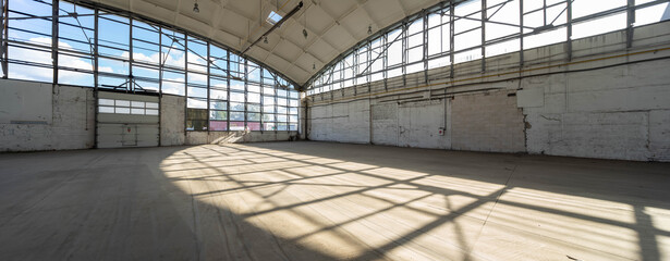 Huge empty industrial warehouse. White interior. Unique architecture. Hemispherical reinforced concrete load bearing roof with windows. Shadow of construction on floor.