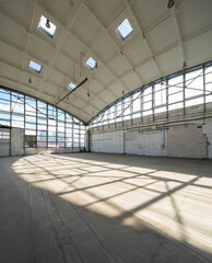 Huge empty industrial warehouse. White interior. Unique architecture. Hemispherical reinforced concrete load bearing roof with windows. Shadow on floor. Daylight.