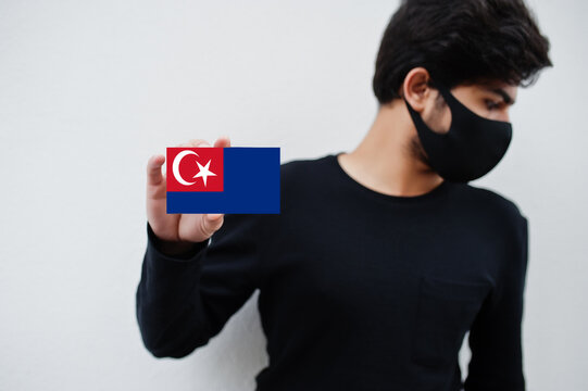 Malay man wear all black with face mask hold Johor flag in hand isolated on white background. States and federal territories of Malaysia coronavirus country concept.