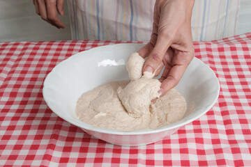Kneading a dough of bread in a bowl. Female hands working. Making pizza. Cooking at home. Homemade food. Italian cloth.