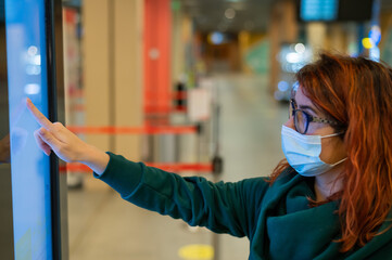 Woman in medical mask uses electronic information board in a public place.
