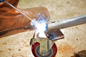 Worker with a welding machine fixing a caster wheels, sparks flying around