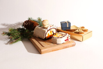 A beautiful Christmas cake, decorated with fir branches with a pine cone and a gift box, on a wooden board. The background is white.