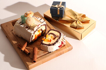 A beautiful Christmas cake, decorated with fir branches with a pine cone and a gift box, on a wooden board. The background is white.