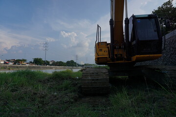 Fototapeta na wymiar Semarang, 15 October 2020; Yellow excavator that stopped at the river bank with a very beautiful blue sky.