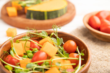 Vegetarian vegetable salad of tomatoes, pumpkin, microgreen pea sprouts on white wooden background. Side view, selective focus.