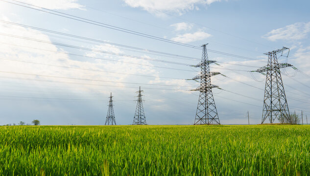 High voltage lines and power pylons and a green agricultural landscape on a sunny day.