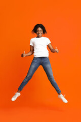 Fototapeta na wymiar African-american joyful lady jumping and showing thumb up