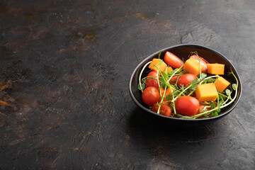 Vegetarian vegetable salad of tomatoes, pumpkin, microgreen pea sprouts on black concrete background. Side view, copy space.