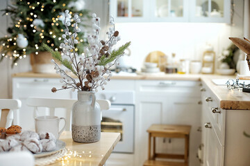 Christmas decorations. Home interior in pastel colors. Cotton branches in a vase on a table. Multi-colored bokeh in the background