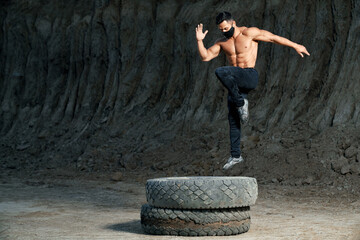 Young shirtless man jumping on large wheel outdoors