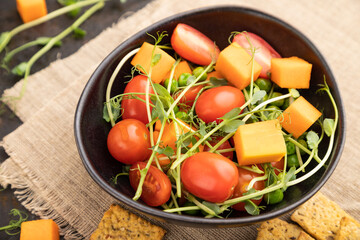 Vegetarian vegetable salad of tomatoes, pumpkin, microgreen pea sprouts on black concrete background. Side view, selective focus.