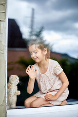 Child girl plays with a British little playful kitten at home windowsil