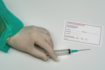 Covid-19 vaccination card medical concept with chemist holding a syringe. Female hand with protective green suit and white gloves next to document for coronavirus protection immunization shot.