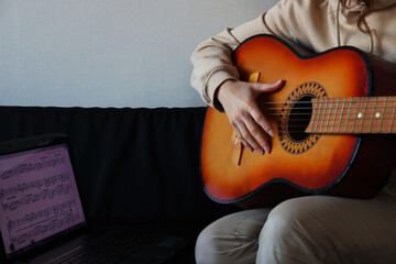 A girl is playing the guitar and watching notes on a laptop. 