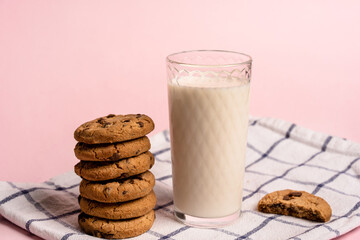 oatmeal chocolate chip cookies and a glass of milk on a checkered towel on a pastel pink background with space for text