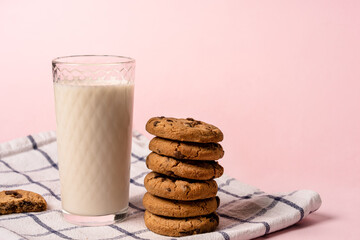 oatmeal chocolate chip cookies and a glass of milk on a checkered towel on a pastel pink background with space for text