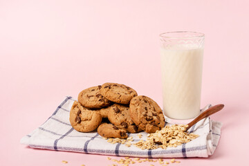 oatmeal chocolate chip cookies and a glass of milk on a checkered towel on a pastel pink background with space for text