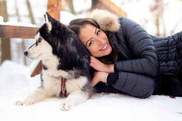 Beautiful young woman hugging female husky dog in cold winter snowy day © MPeev