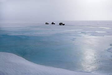 3 cars drive along of a snow covered ice desert, concept of off-road traveling in extreme conditions, copy space, winter landscape or background in white and blue tones