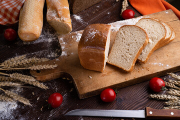 assortiment of tasty fresh  bread. served at  wooden table with cherry tomatos and wheat ears.